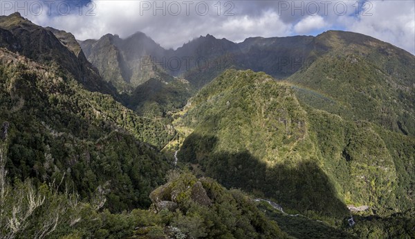Densely overgrown steep mountains with rainbow, green mountain landscape, view from Miradouro dos
