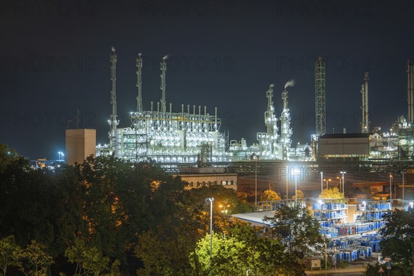 Industrial end at night with illuminated chimneys and warehouse buildings surrounded by trees and