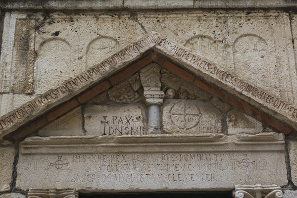 Close-up of carved letters and ancient symbols on old limestone building facade with triangular