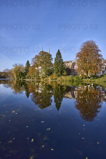 Mill pond with trees, general buildings against a cloudless blue sky, symmetrical reflections on