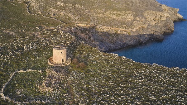 Drone shot, Lindos, late afternoon light, drone view of an old windmill on a rocky shore in the