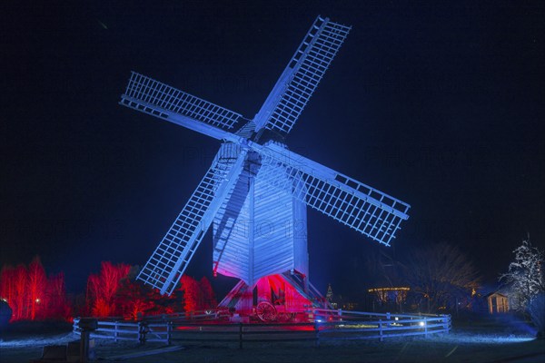 A large, blue-red illuminated windmill at night with a dark background, world of lights,