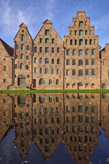 Historic salt warehouses, brick buildings reflected on the water surface of the Trave, blue sky