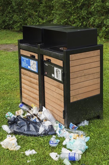 Black painted metal and natural wood garbage recycling bins with discarded thrash on green grass