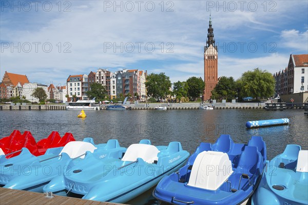 Colourful pedal boats on the river, buildings and a striking tower in the background, St. Nicholas
