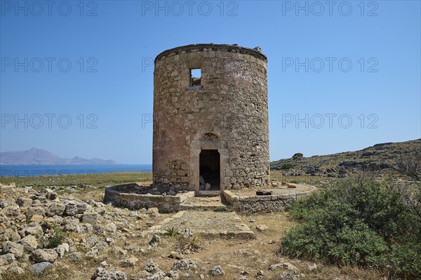 Old, abandoned mill near the coast, surrounded by rocky terrain under a blue sky, windmill, ruin,