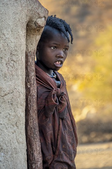 Himba girl leaning against a traditional mud hut, in the morning, traditional Himba village,
