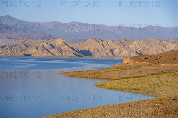 Blue Toktogul reservoir between dry mountain landscape, hilly mountains in the evening light,
