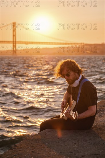 Hipster street musician in black playing electric guitar in street outdoors on sunset