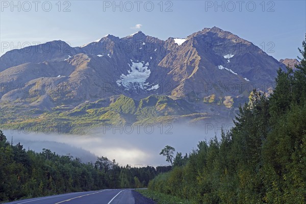 Traffic-free road leads as grades towards rough, snow-covered mountains, morning fog in autumn,