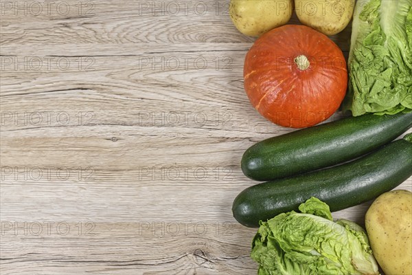 Healthy raw Hokkaido squash, zucchini, lettuce and potatoes on side of wooden background with empty