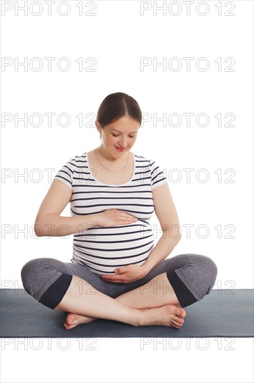 Pregnancy yoga exercise, pregnant woman doing asana Sukhasana easy yoga pose embracing her belly