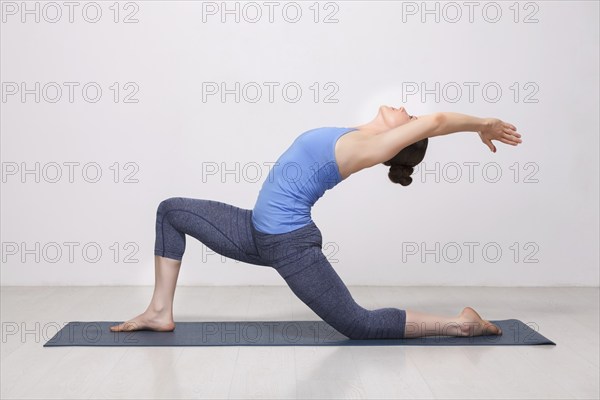 Beautiful sporty fit yogini woman practices yoga asana Anjaneyasana, low crescent lunge pose in