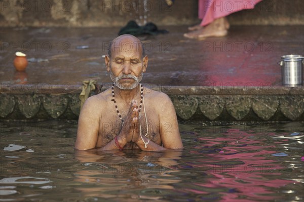 Indian man bathing and praying in the Ganges river at a ghat at Varanasi, Uttar Pradesh, India,