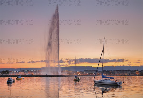The Jet d'eau at dusk is the landmark in the Lake Geneva basin, with sailboats in the foreground