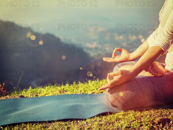 Close up of woman in Padmasana yoga lotus pose with chin mudra outdoors with copyspace. With light