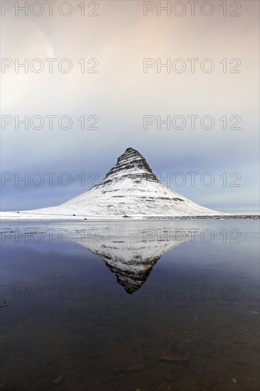 Kirkjufell, nunatak hill covered in snow reflected in water of fjord on the Snæfellsnes peninsula