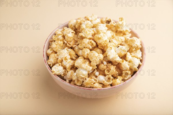 Popcorn with caramel in ceramic bowl on pastel orange background. Side view, close up