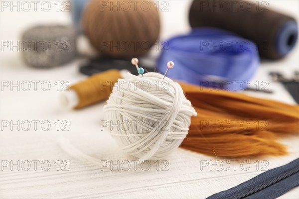 Sewing accessories: scissors, thread, thimbles, braid on white wooden background. Side view, close