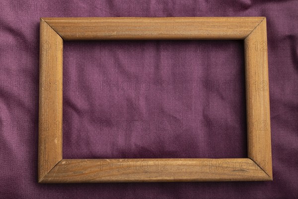 Wooden frame on smooth cotton purple tissue. Top view, flat lay, natural textile background and