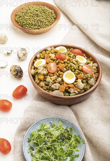 Mung bean porridge with quail eggs, tomatoes and microgreen sprouts on a white wooden background