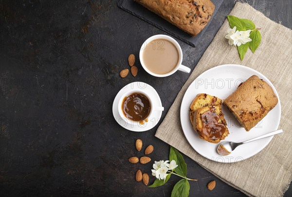 Homemade cake with raisins, almonds, soft caramel and a cup of coffee on a black concrete
