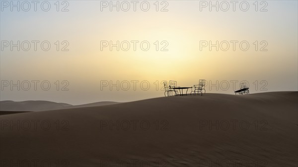 Sunset, cast iron table and chairs in the sand dunes of Erg Chebbi, Sahara, Merzouga, Morocco,