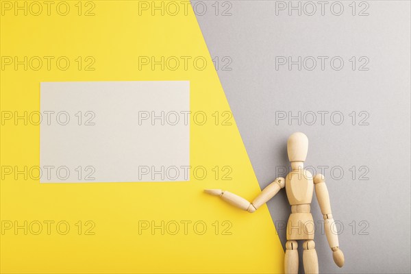 Wooden mannequin holding gray blank poster on gray and yellow pastel background. copy space,
