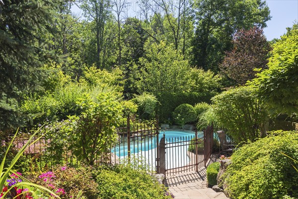In-ground swimming pool surrounded by copper coloured wrought iron metal security fence and various
