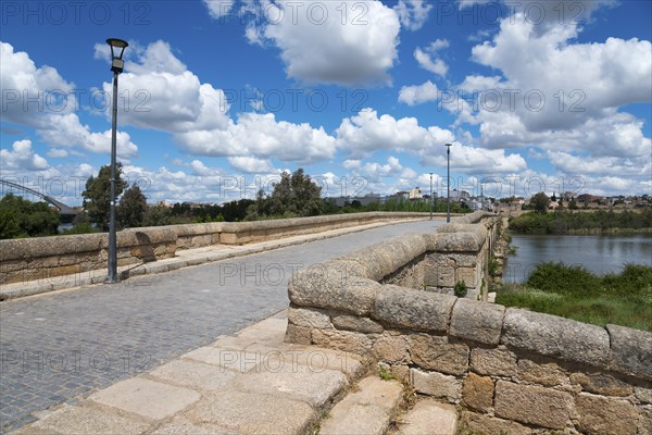 View of an old stone bridge with cobblestones against a clear blue sky and white clouds, Roman