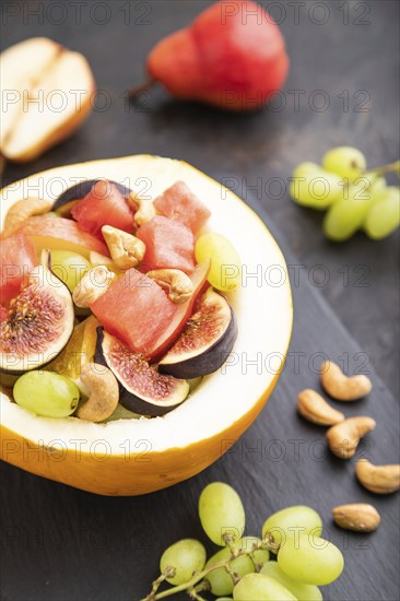 Vegetarian fruit salad of watermelon, grapes, figs, pear, orange, cashew on slate board on a black