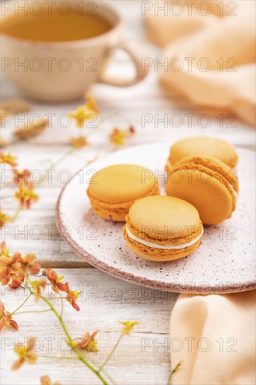 Orange macarons or macaroons cakes with cup of apricot juice on a white wooden background and