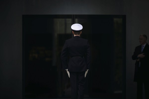 A marine stands with his back to the camera in front of the entrance to the Federal Chancellery.