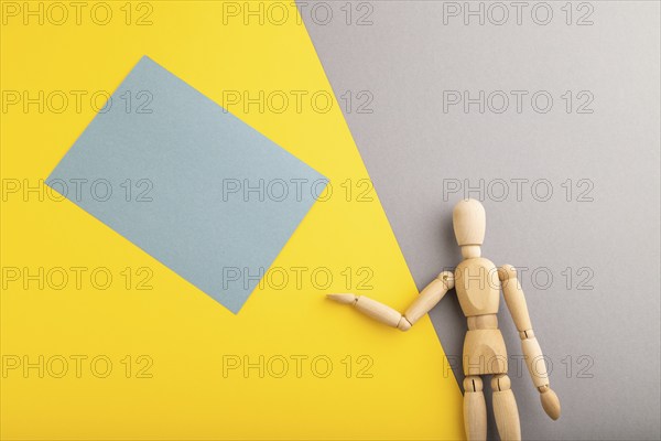 Wooden mannequin holding blue blank poster on gray and yellow pastel background. copy space,