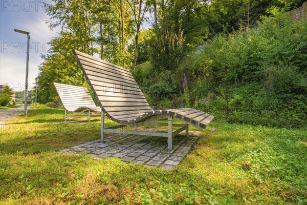 Several wooden loungers in a sunny park surrounded by green vegetation, Nagold, Black Forest,