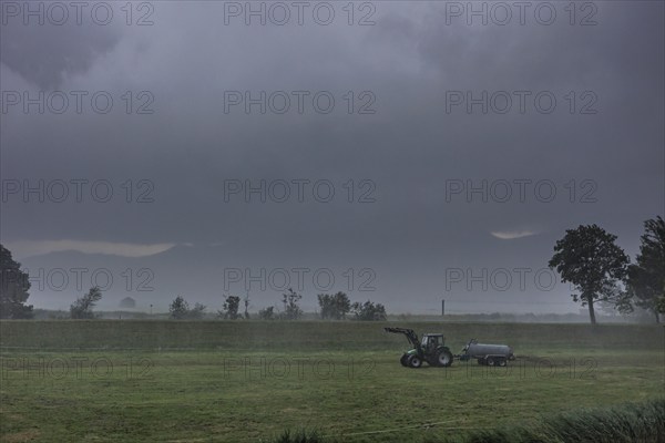 A farmer drives slurry onto a meadow with his tractor in the rain, storm, thunderstorm, Schlehdorf,