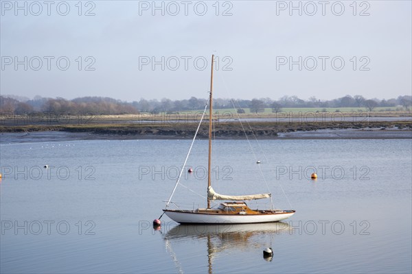 One yacht moored off muddy shore calm water River Deben, Waldringfield, Suffolk, England, UK