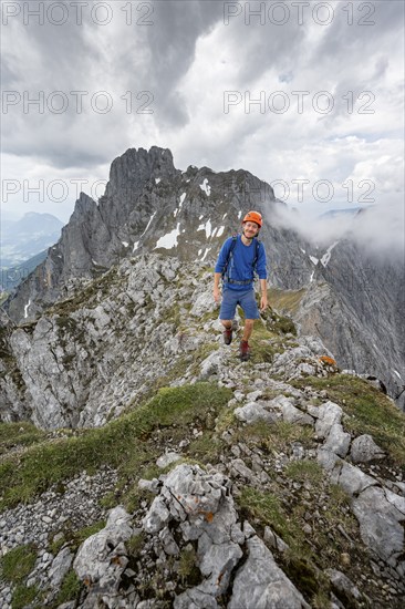 Mountaineer with helmet on a narrow hiking trail on a rocky ridge, ascent to the Maukspitze, clouds