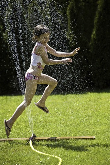 Young girl refreshing herself under a lawn sprinkler, Federal Republic of Germany