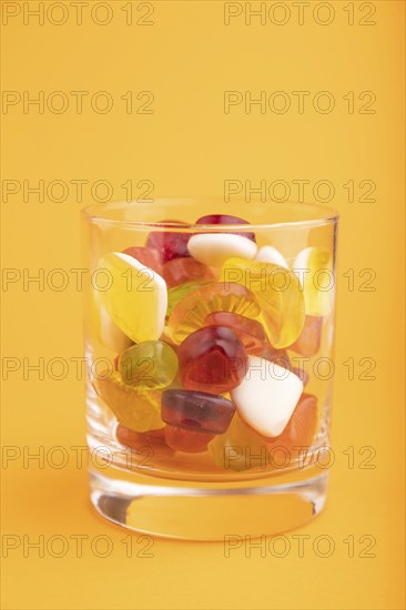 Various fruit jelly candies in drinking glass on orange pastel background. side view, close up