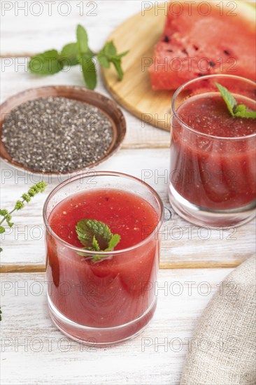 Watermelon juice with chia seeds and mint in glass on a white wooden background with linen textile.