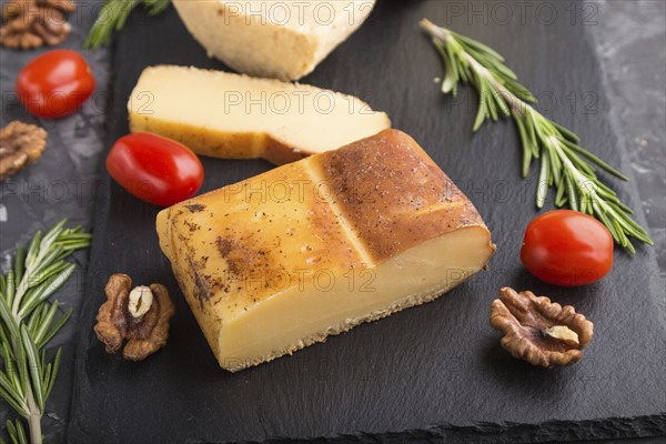 Smoked cheese and various types of cheese with rosemary and tomatoes on black slate board on a