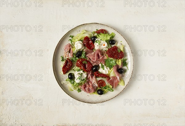 Salad with dried tomatoes, prosciutto, soft cheese, olives, homemade, top view