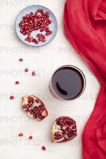 Glass of pomegranate juice on a white concrete background with red textile. Top view, close up,