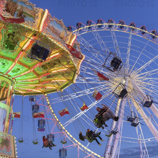 Illuminated chain carousel and Ferris wheel at night with cheerful people, funfair, wave flight,