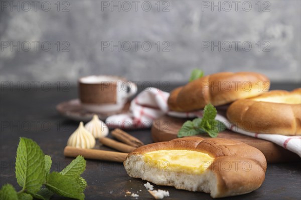 Sour cream bun with cup of coffee on a black concrete background and linen textile. Side view,