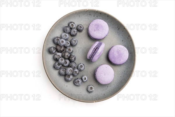 Purple macarons or macaroons cakes with blueberries on ceramic plate isolated on white background.
