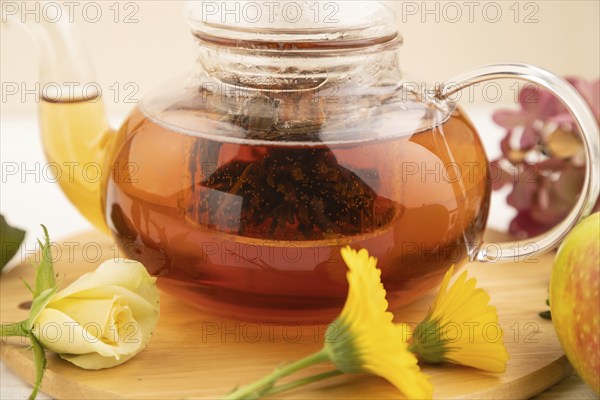 Red tea with herbs in glass teapot on white wooden background. Healthy drink concept. Top view,