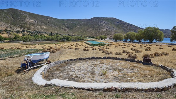 Rural scene with a field, a boat, mountains and some scattered trees, bales of straw, Old threshing