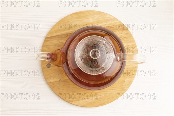 Red tea with herbs in glass teapot on white wooden background. Healthy drink concept. Top view,